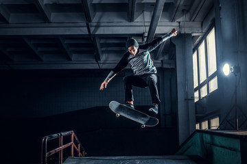 Skateboarder jumping high on mini ramp at skate park indoor. - obrazy, fototapety, plakaty