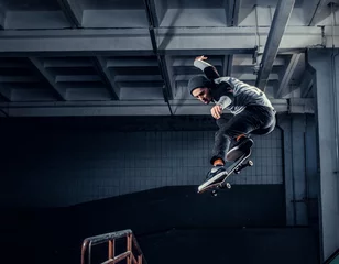 Rolgordijnen Skateboarder jumping high on mini ramp at skate park indoor. © Fxquadro