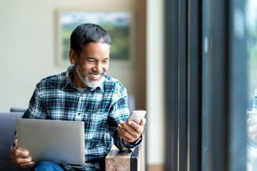 Candid of old asian retired man using mobile phone to transfer money online or financial payment and read text, smile or laugh with happy and positive. Senior asian with digital technology concept.