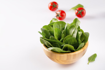 Fresh baby spinach in a wooden bowl on white background.