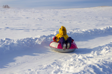 Fototapeta na wymiar The girl rides a tubing down the snowy road, winter sport.