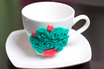 Fototapeta na wymiar Mug, decorated with flowers made of polymer clay. Crafts from polymer clay. Mug decorated with stucco made of polymer clay