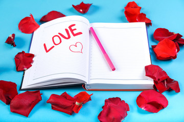 The word love written in red felt-tip pen in a notebook on a blue background in the design of rose petals.