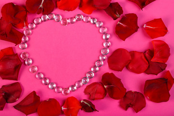 Heart of beads on a pink background decorated with rose petals.
