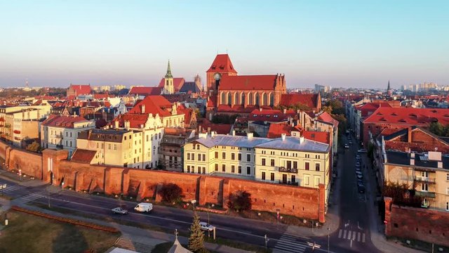 Torun old city in Poland. Aerial revealing 4K video in sunrise light with medieval Gothic St John Cathedral, town hall tower, Vistula river, historic buildings, town walls and gates