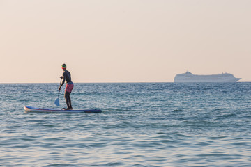 Man on stand up paddle watching a cruise ship in background
