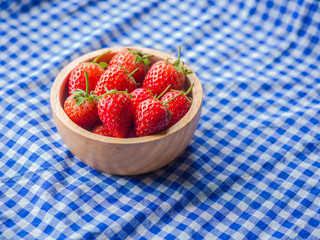 Strawberry in a wooden cup on blue and white checkered fabric texture.