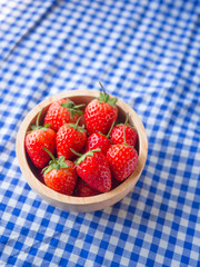 Strawberry in a wooden cup on blue and white checkered fabric texture.