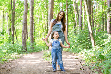 Fototapeta premium Family, nature and people concept - Mother and cute little daughter spend time together on a walk in the forest