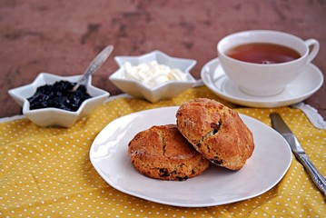 Traditional English scones with dried cranberries on a white plate. Served with jam and whipped cream.