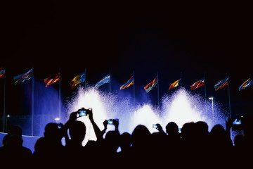 Fototapeta na wymiar People shoots fountain and flags on smartphones. People silhouettes. Night