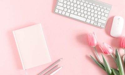 Home office pink table, notepad, clipboard, keyboard, flowers, diary, notebook, stationery on pink...