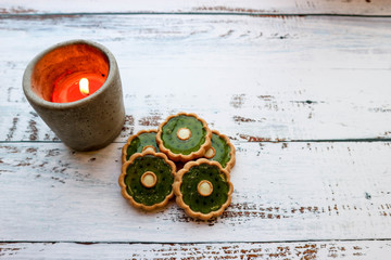 Christmas gift card, orange burning candle and decorations of green cookies on wooden background