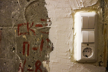  White plastic double light switch on the old black and white plastered concrete wall, process of renovation