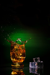 A glass of whiskey on a beautiful green background and a splash from falling ice