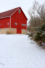Winter rural landscape with red barn.Snowy winter view with old red barn.Old style stoned red barn and yard covered by snow close up.Wisconsin, Midwest USA rural life at winter and farming background. © Maryna