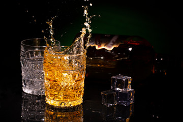 Two crystal glases of whiskey on a beautiful black background and a splash from falling ice