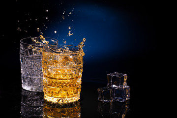 Two crystal glases of whiskey on a beautiful blue background and a splash from falling ice