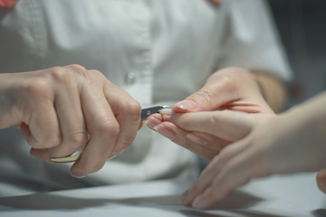 Manicurist master is cutting the length of nails with nail clippers. Nail care concept.