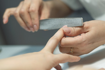 Obraz premium Manicurist polishes fingernails with manicure file. Nail preparation for nail polish.