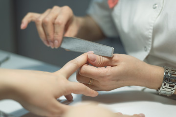 Obraz na płótnie Canvas Manicurist polishes fingernails with manicure file. Nail preparation for nail polish.