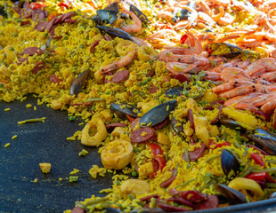 Street food in France, fresh prepared paella with rice and sea food in big pan on street market, ready to eat