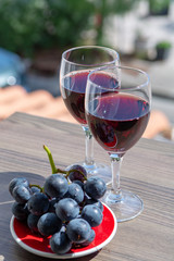 Two wine glasses with red wine served with red grape on outdoor terrace