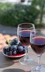Two wine glasses with red wine served with red grape on outdoor terrace