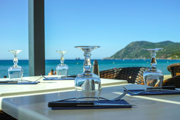 Fototapeta premium Elegant cafe with sea view on French Riviera is waiting for guests, served lunch table with glasses, tableware and napkins
