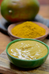 Tasty mango-curry sauce in small bowl ready to eat and bowls with mango and curry powder close up