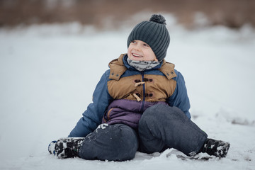 Fototapeta na wymiar Six year old boy smiling and sitting on snow.
