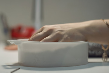 Woman softens her nails in a warm bath in the salon. Fingernail care.