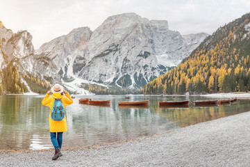 Fototapeta na wymiar Asian woman traveler on the shore of the famous tourist lake Braies in the Dolomites Alps, Italy. The concept of travel and adventure in the mountains at autumn season
