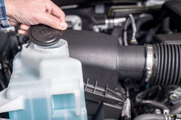 Man removes the plastic cap from the windshield washer fluid container in a truck