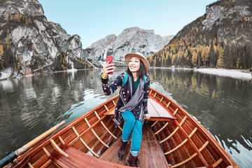 Happy asian woman taking selfie with smartphone in a boat in a mountain lake during fall season