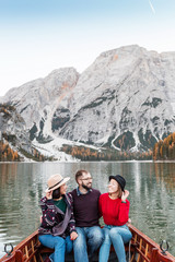 Group of three happy travelers on a wooden Boat on a lake in the mountains. Vacation and tourism in Italian Dolomites concept