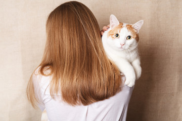 Gentle white cat on a woman's shoulder. White cat on the shoulder of a blonde on a beige background