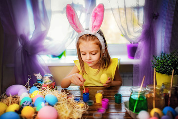 Obraz na płótnie Canvas colorful painted eggs, flowers in vase. Happy easter girl in bunny ears having fun and painting eggs. small child at home. spring holiday
