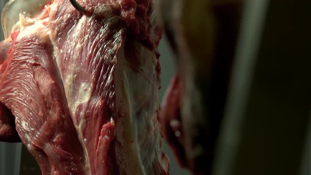 Close up view of raw meat hanging in a refrigerator. Peeled cows head hanging on hook at slaughterhouse. Organic meat manufacture.