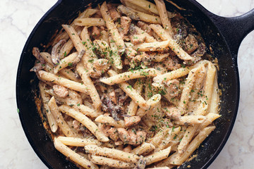 homemade italian creamy pasta with forest mushrooms and chicken fillet in a pan top view