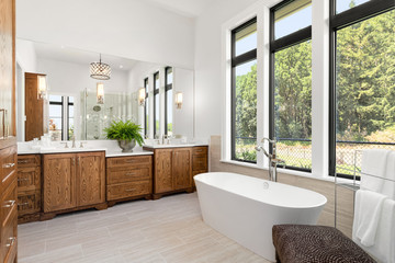 Beautiful bathroom in new luxury home, with double vanity, bathtub, and shower visible in mirror reflection.