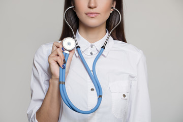 Young female doctor in uniform with stethoscope. Gray background.