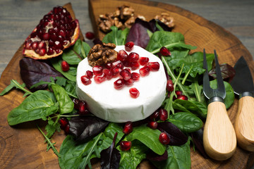 Soft Camembert cheese, pomegranate grains and mix salad with young spinach, arugula, beet leaves on a brown wooden board. Tasty, gourmet food