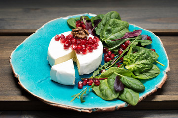 Soft Camembert cheese, pomegranate seeds & mix salad with young spinach, arugula, beet leaves, on a blue plate. Tasty, gourmet food