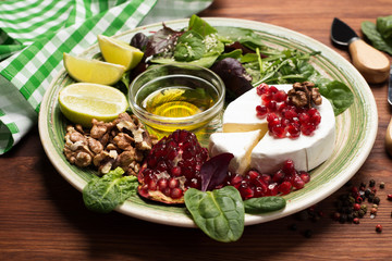 Soft Camembert cheese, pomegranate seeds, mix salad with young spinach, arugula, beet leaves, lime and nuts on a green plate. Tasty, gourmet food