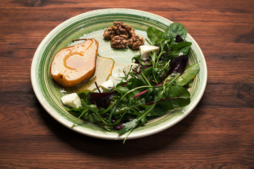 Pear, stewed in honey, mix salad with young spinach, arugula, beet leaves, blue cheese, walnuts on a green plate on a wooden board. Delicious, gourmet salad