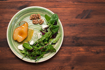 Pear, stewed in honey, mix salad with young spinach, arugula, beet leaves, blue cheese, walnuts on a green plate on a wooden board. Delicious, gourmet salad