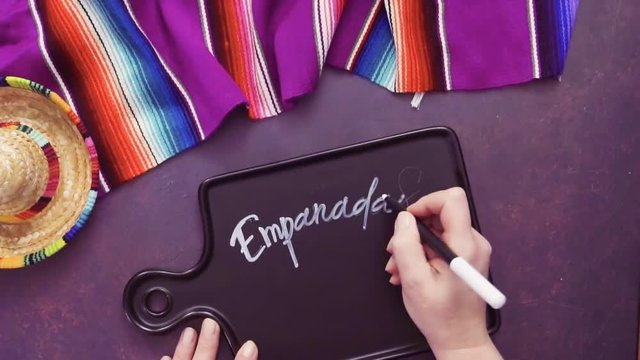 Flat lay. Writing Emapanadas sign on black chalk board.