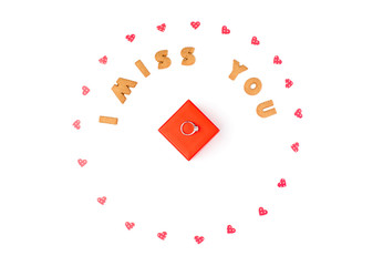 Valentine's day concept. Text I MISS YOU from cookies, frame made of paper hearts. In the center red gift box with ring. Flat lay, top view, white background, isolated, copy space