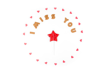 Valentine's day concept. Text I MISS YOU from cookies, frame made of paper hearts. In the center lollipop in form star. Flat lay, top view, white background, isolated, copy space